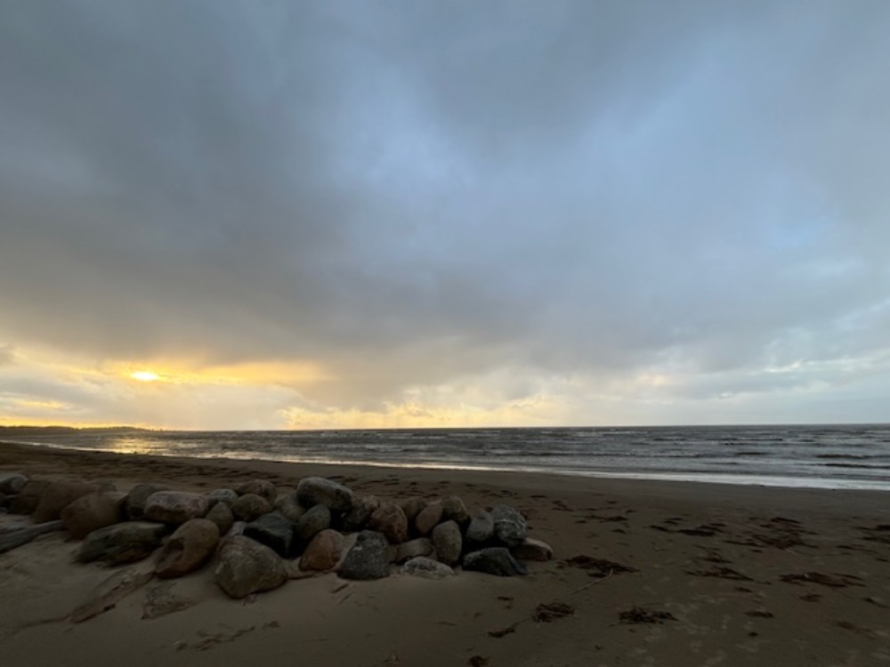 Stones on Kabli beach under a cloudy sky with the sun breaking through, symbolizing hope and Zen resilience in trauma healing.